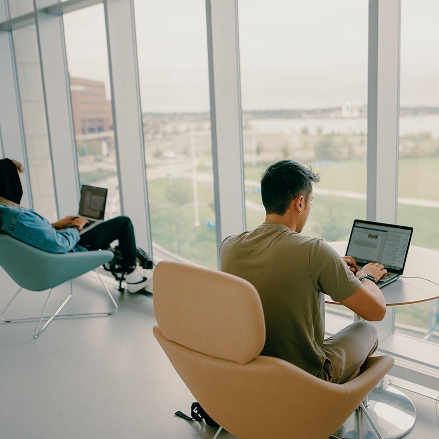 Student on laptop in chair in Uhall balcony facing window.